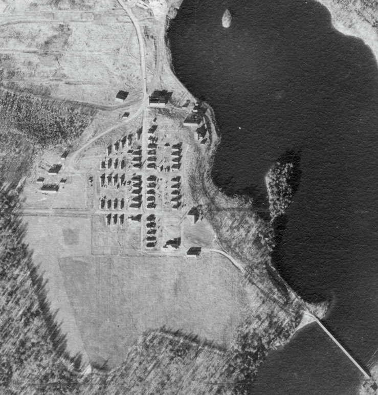 Photo: Black and white aerial photo of a small town, showing buildings and fields.