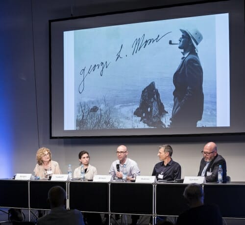 Photo: Panelists sitting beneath projected photo of Mosse