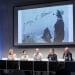 Photo: Panelists sitting beneath projected photo of Mosse