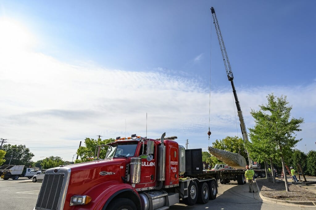 Photo: A crane lowers a huge statue onto a large track.