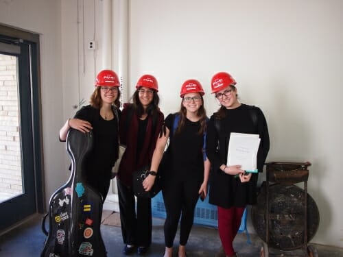 Four women in construction hats pose with their instruments.