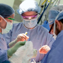 Photo: Surgeons in scrubs standing around a patient during an operation