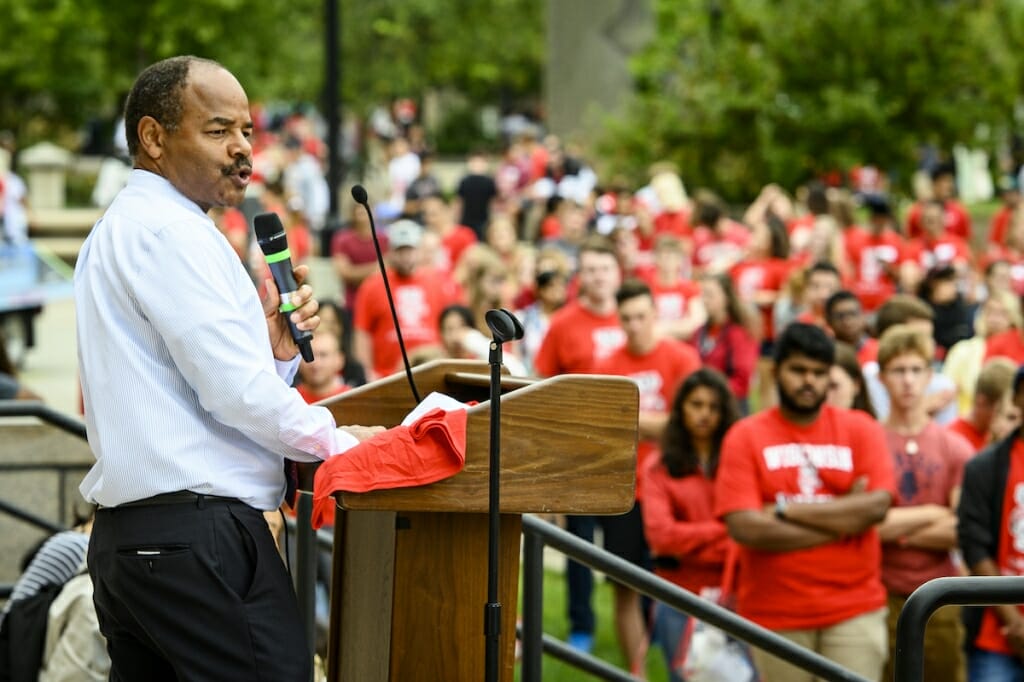 Photo: A man speaks at a podium to red-clad students.
