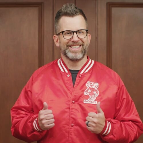 Photo: Gay standing in an elevator in a red Badger jacket giving 2 thumbs up