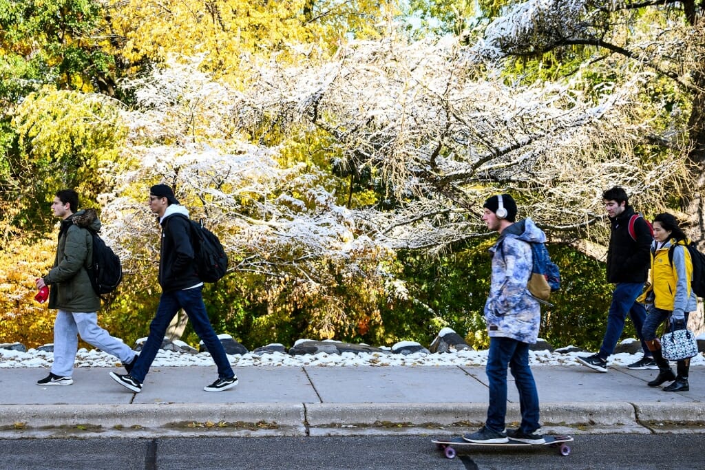 Photo: Pedestrians walk and ride skateboards in the snowy landscape.