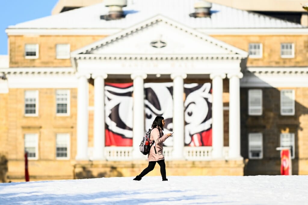 Photo: A woman walks across a snow-laden path, with Bascom Hall behind her.