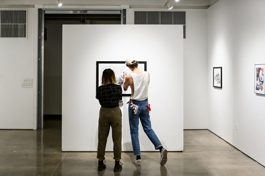 Photo: Two people closely examine an artwork.