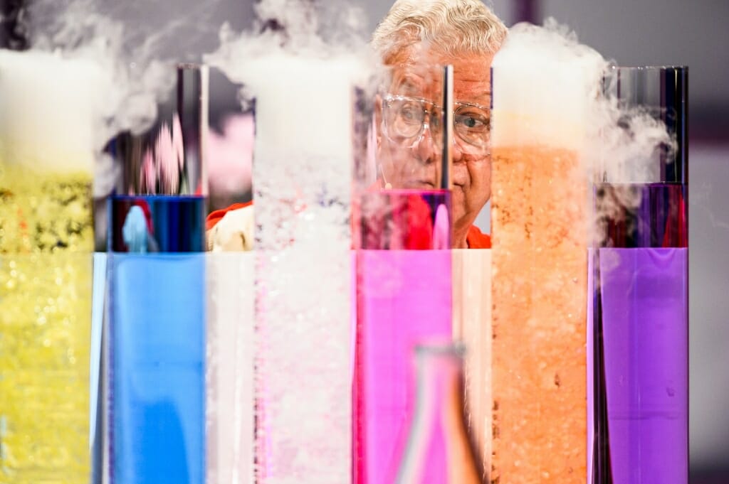 Photo of Shakhashiri seen through brightly colored cylinders of chemicals.