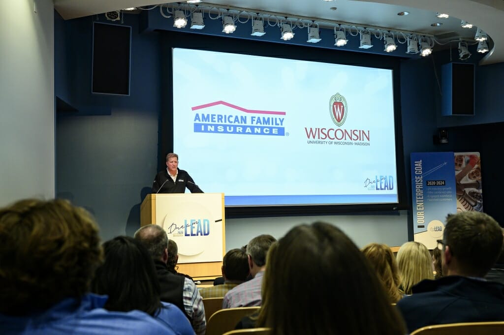 Photo: Dan Kelly speaking at a podium next to a screen with American Family and UW logos