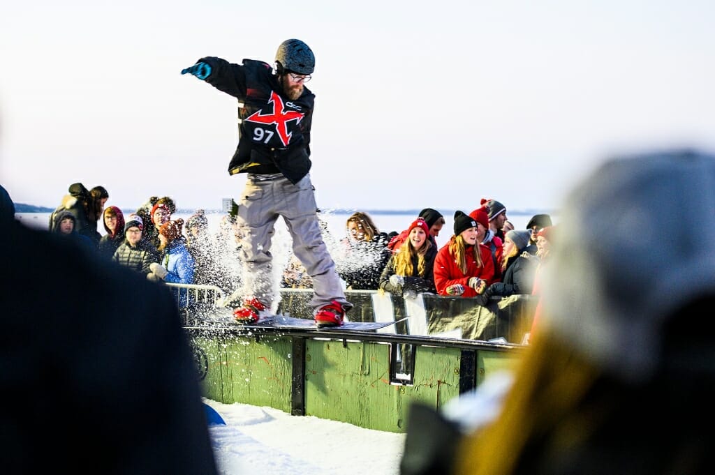 A snowboarder, hands raised to balance himself, slides along a rail.