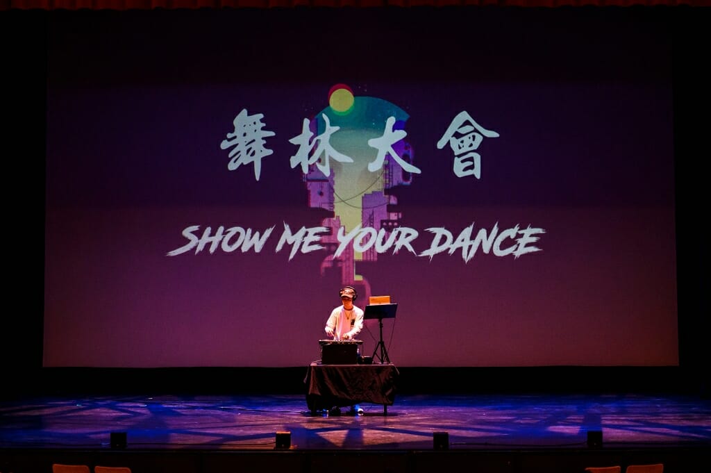A performer in front of a projected sign saying 