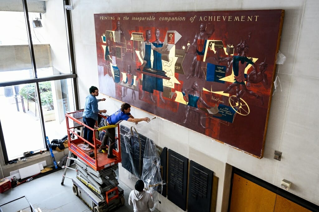 Workers pull plastic bits off the frame of the mural.