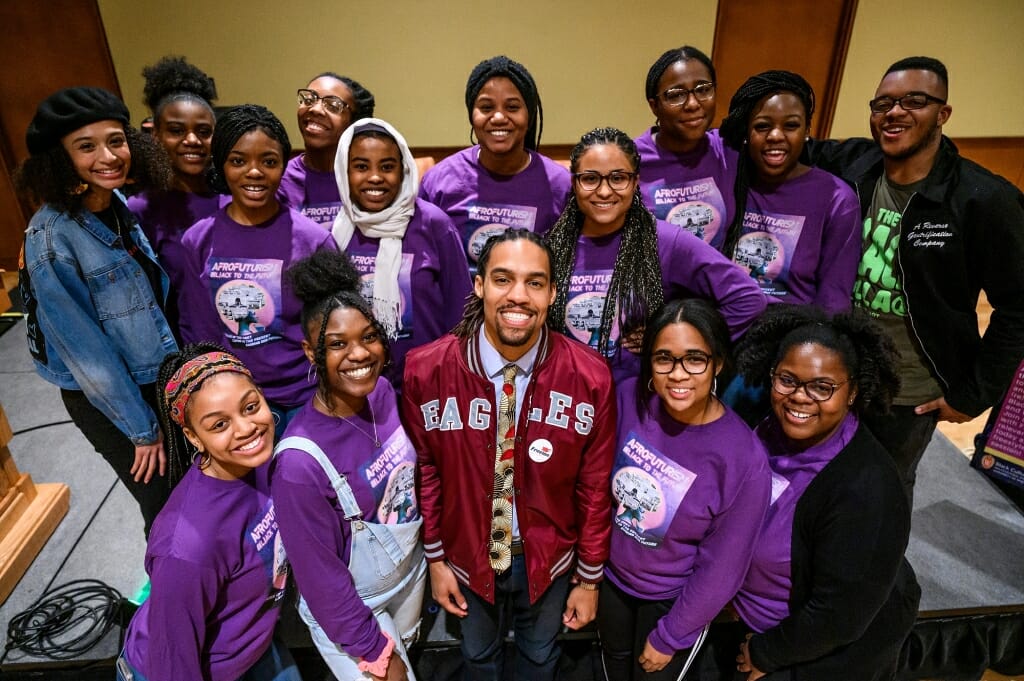A photo of the 2020 Black History Month planning committee wearing matching purple shirts and standing with their Keynote Speaker, Freelon.