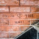A brick wall has a heart sketched and the words 