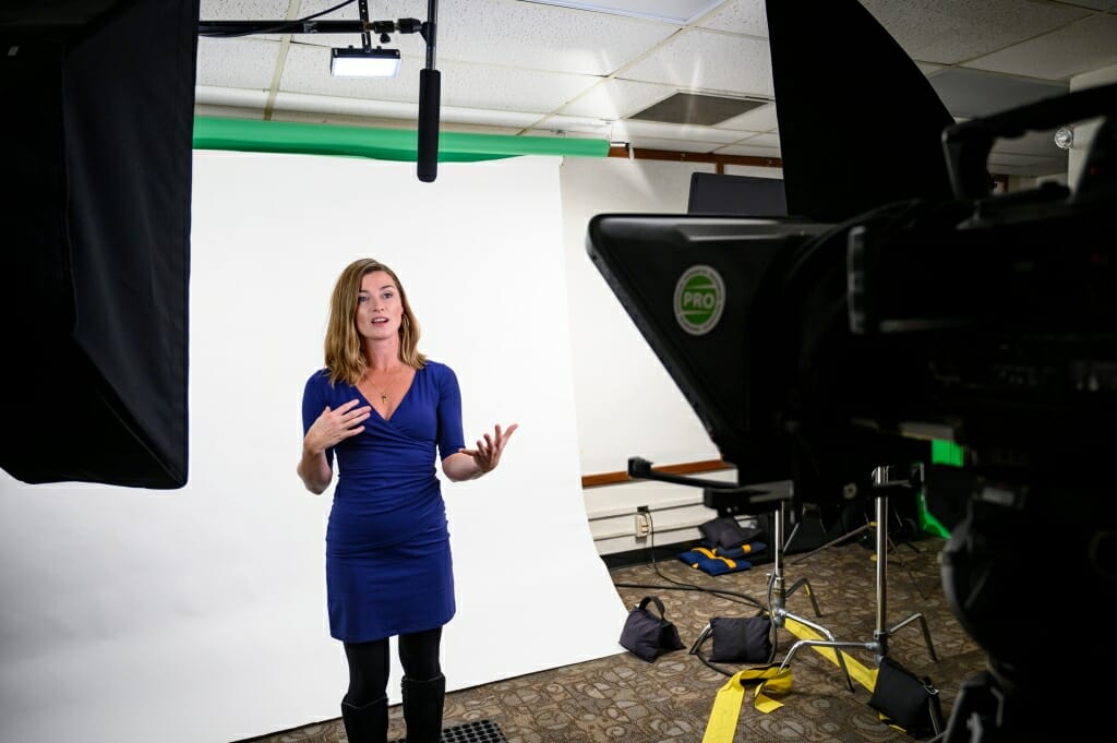 Sara McKinnon standing in front of a white background, speaking into a video camera