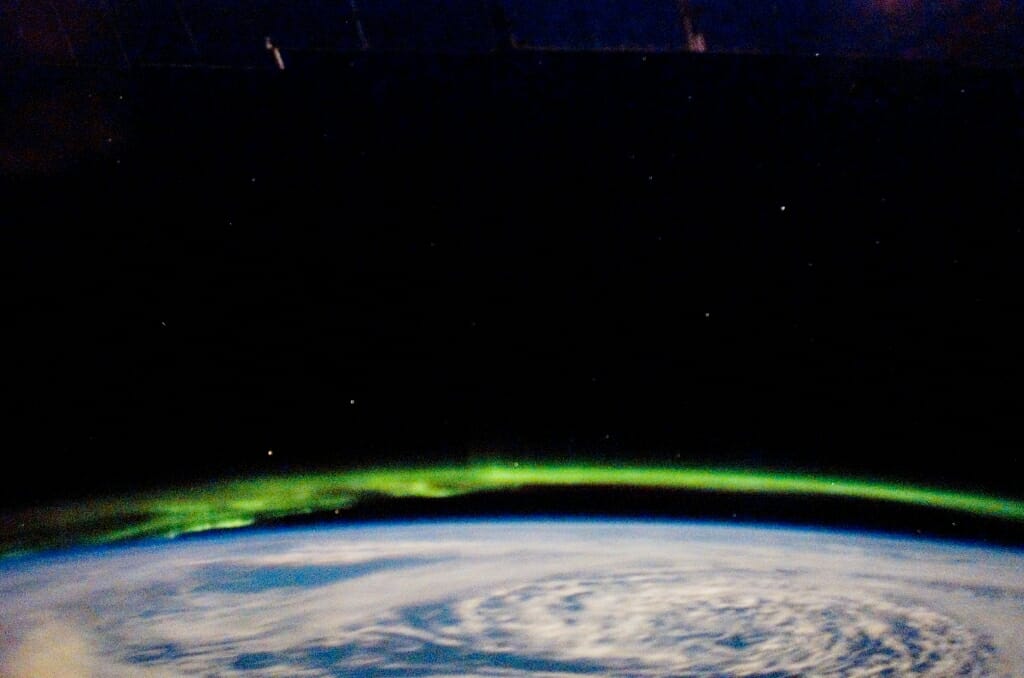 Green corona seen above cloud-covered Earth against black sky