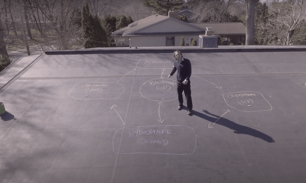 A professor stands on a chalked rooftop to teach his class.
