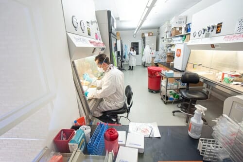 Man in white lab coat, face mask and rubber gloves working in laboratory