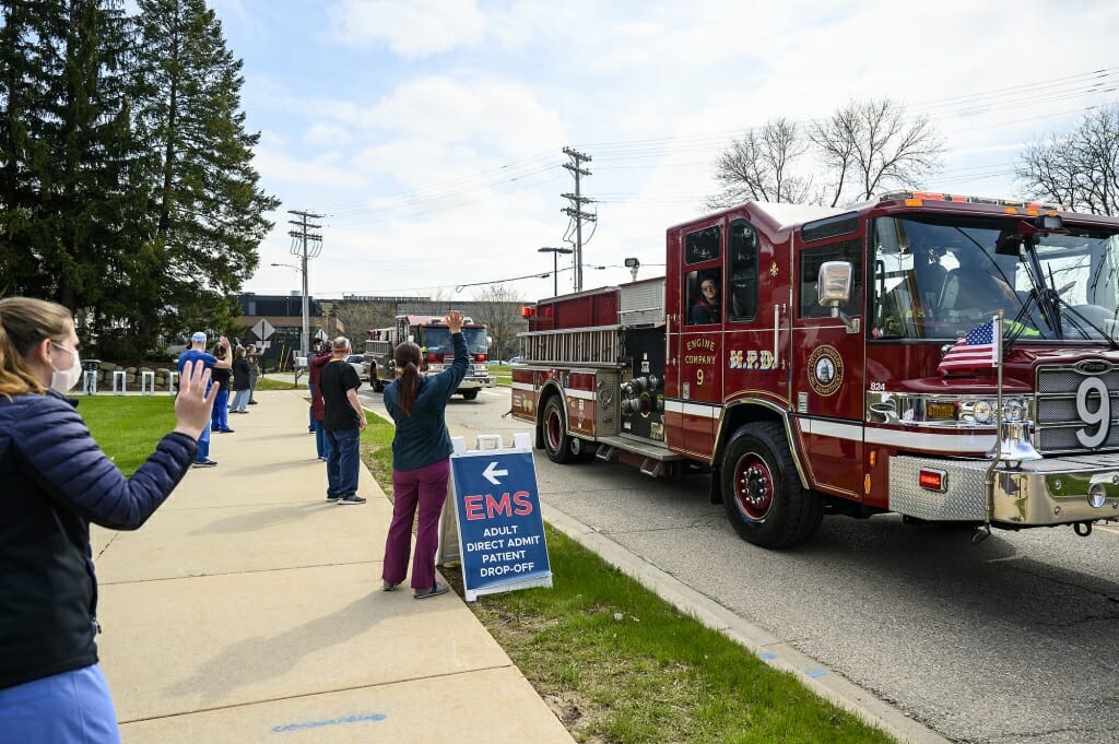 Health care workers standing on sidewalk waving at passing fire engine