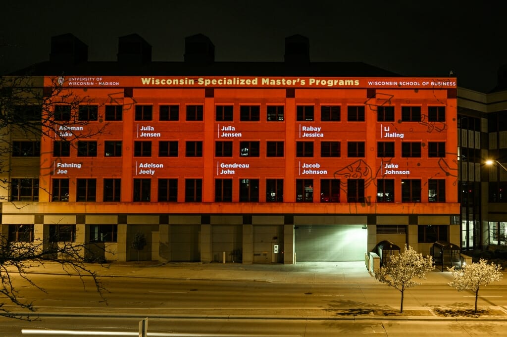 A night time shot of a building with red light projected upon it, with names in white.