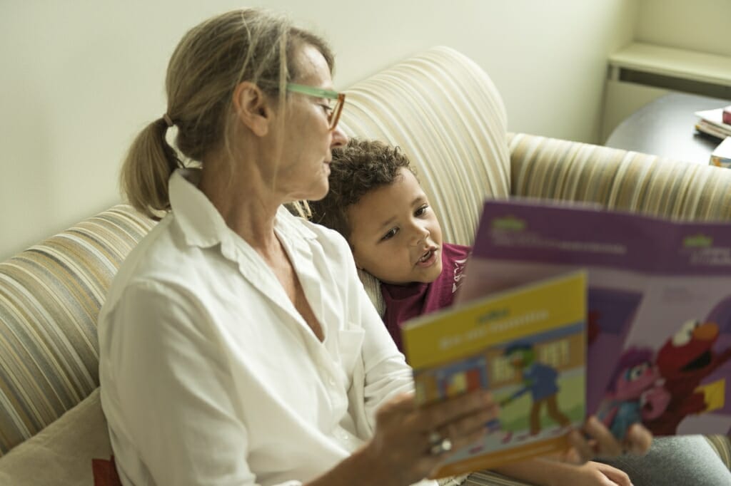 A woman and a young child sit on a couch and look at a book.