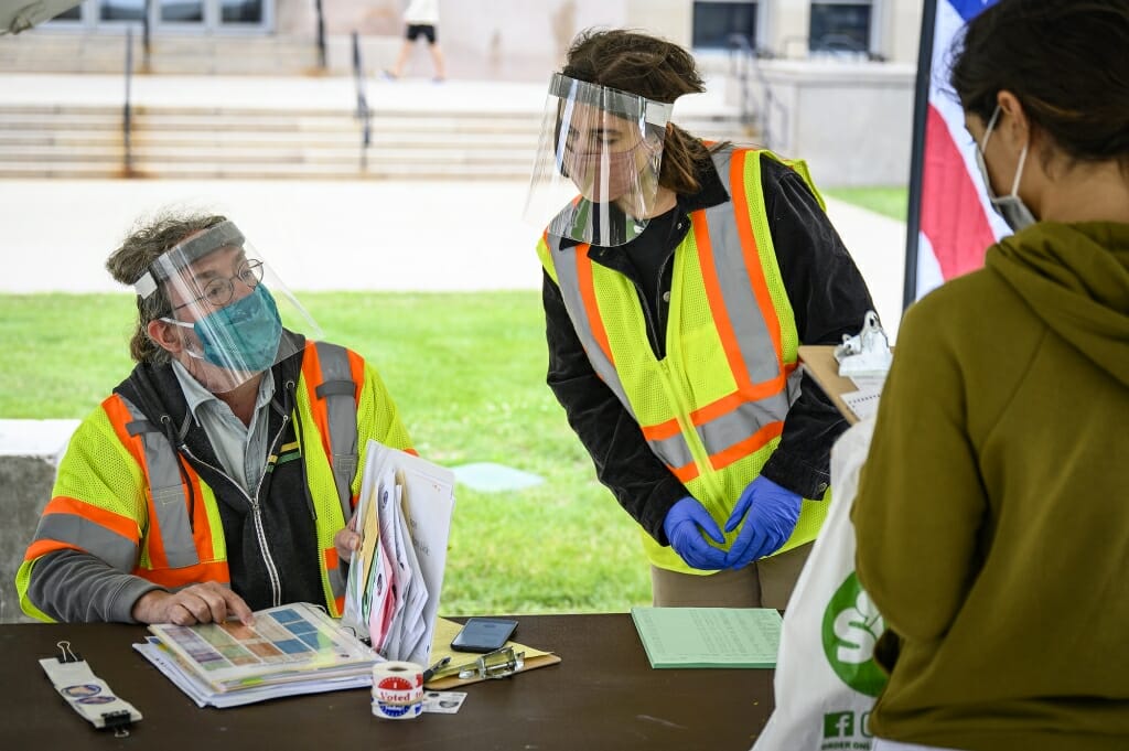 Poll workers Greg Smith (left) and Alexis Sutherland (right) help a voter during in-person absentee voting for the August primary election. Similar outdoor tents will be set up for in-person absentee voting for the Nov. 3 presidential election.