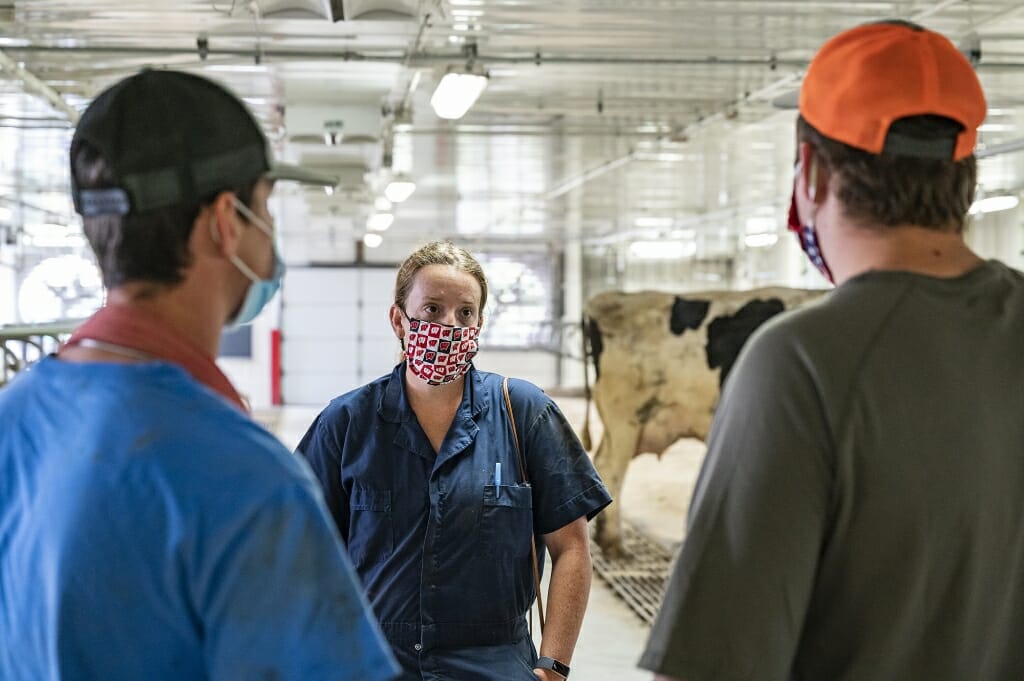 3 people standing and talking inside milking parlor