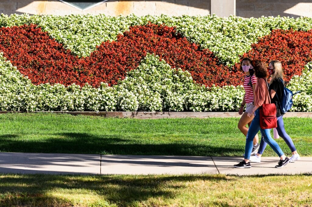 Pedestrians walk past a W-shaped flower bed in front of Mosse Humanities Building.