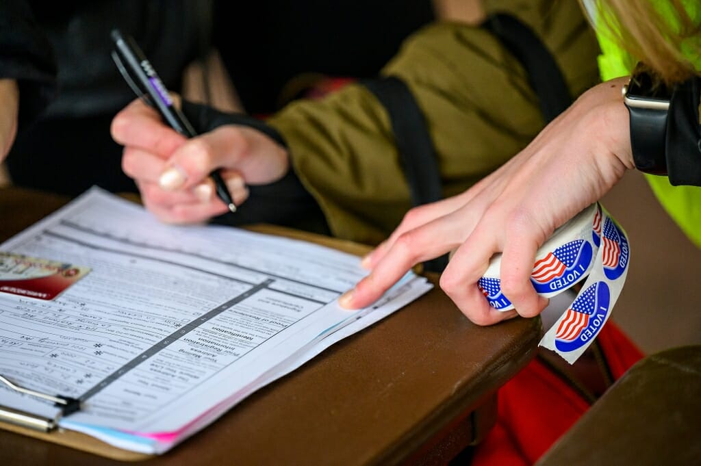 A staff member from the City of Madison Clerk’s Office, right, signs a student’s registration to vote. The tents offer voter registration as well as voting.