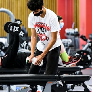 A student sanitizes a weight bench as he works out in the strength equipment area.