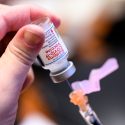 Closeup of a person's fingers holding a vial of vaccine being drawn into a needle