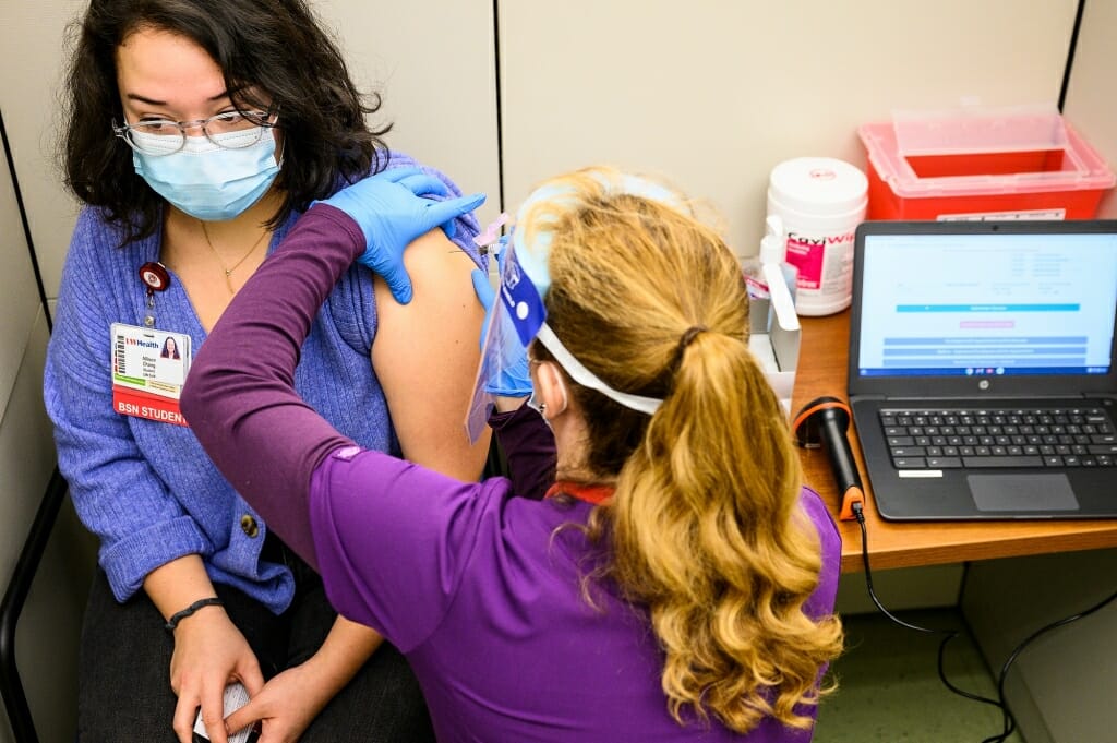 A person wearing rubber gloves injecting a vaccine into a person's arm
