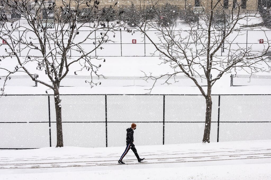 A pedestrian walks along Observatory Drive as a late winter snow storm blankets campus.
