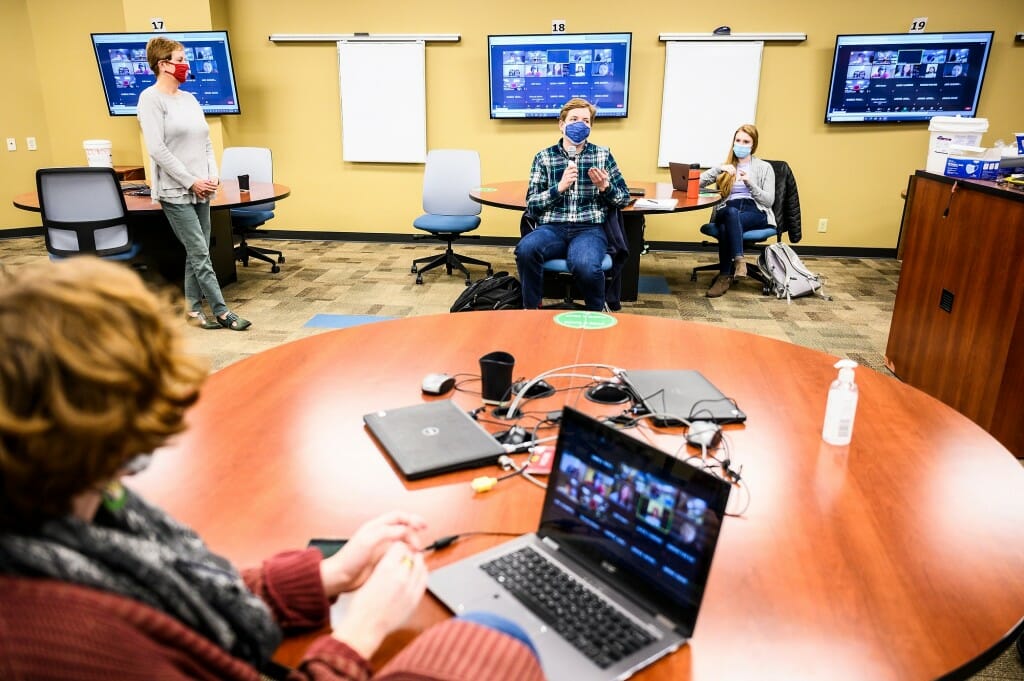 At center holding a sanitized microphone, student Thomas Lavery shares a thought during Anthropology 490: Climate, Environment and Landscape, taught by Professor Sissel Schroeder (pictured standing at upper left) in Grainger Hall on March 3. Approximately two-thirds of the students in this hybrid class attend in-person while one-third participate remotely. 