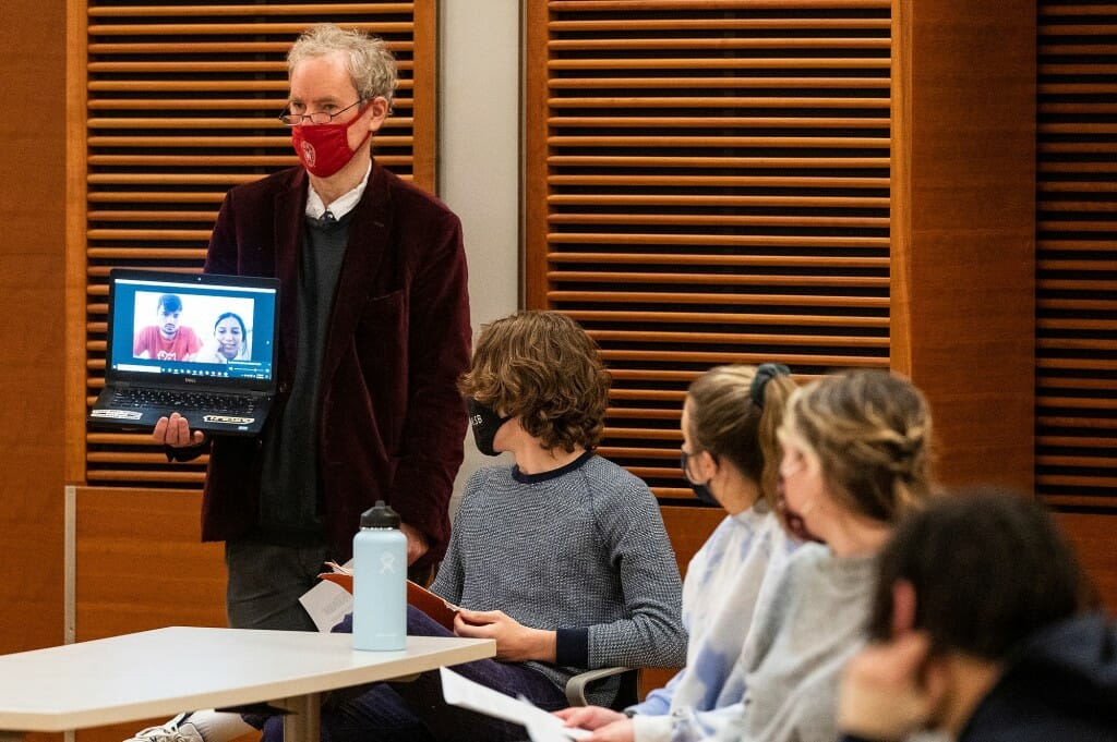 Professor Harry Brighouse holds a laptop displaying two virtual participants as students hold a discussion for Philosophy 304: Topics in Philosophy at the Discovery Building on March 16.