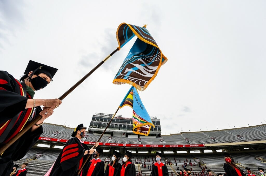 At center, a flag bearer holds the blue Graduate School banner with stripes representing other schools and colleges.