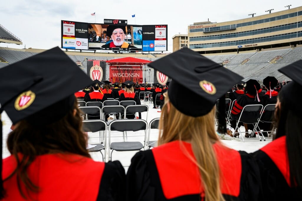 A video of Gottman's speech is displayed on the big screen as graduates watch in the foreground.
