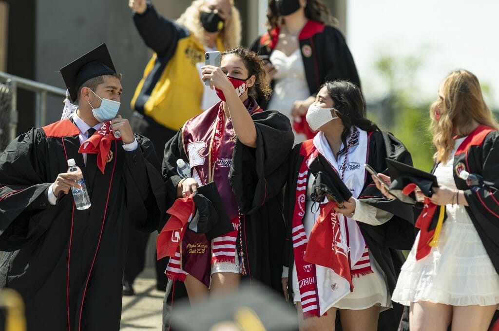 Photo of graduates posing for a selfie as they walk.