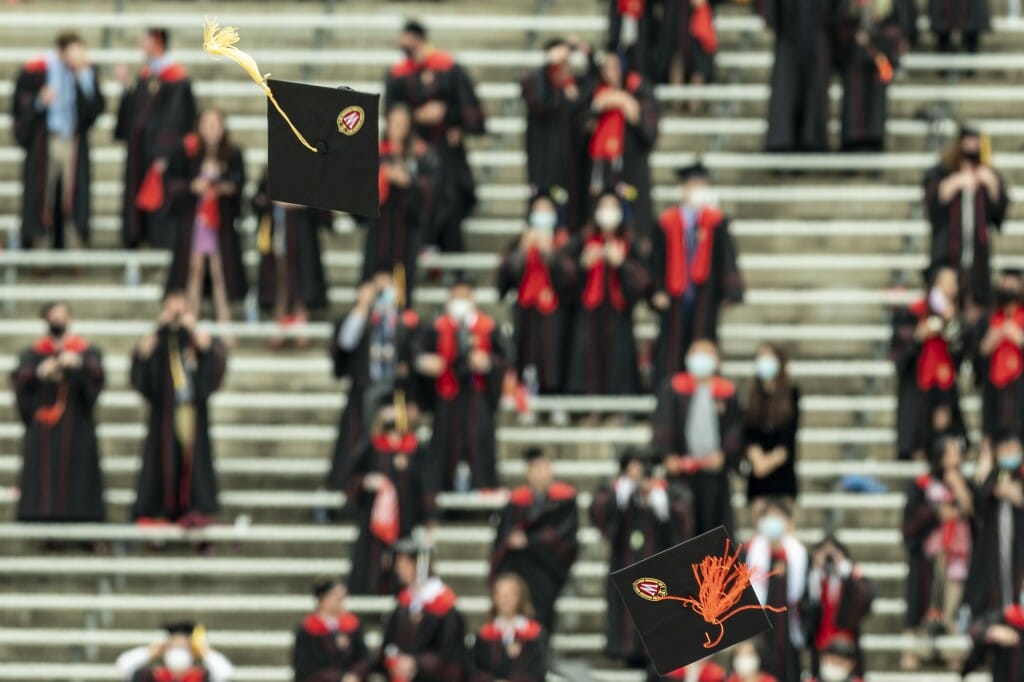 Caps fly in the air as graduates are pictured in the stands behind.