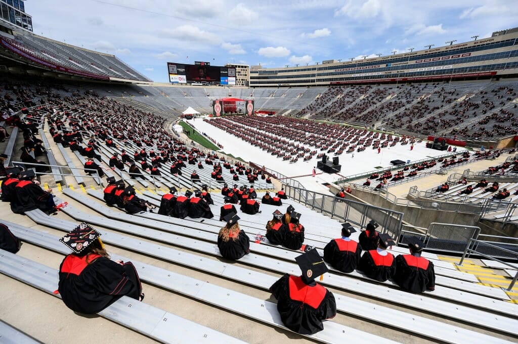 Photo showing groups of graduates spread out in the stands and on the field.