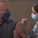 Nursing student administering vaccination to man wearing mask