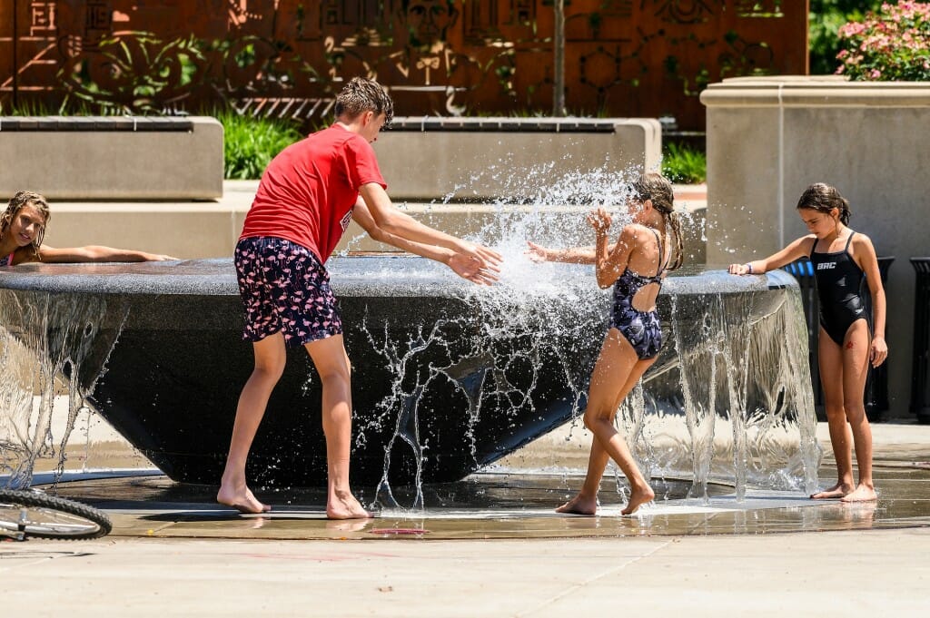 A boy splashes a girl with water from the fountain.
