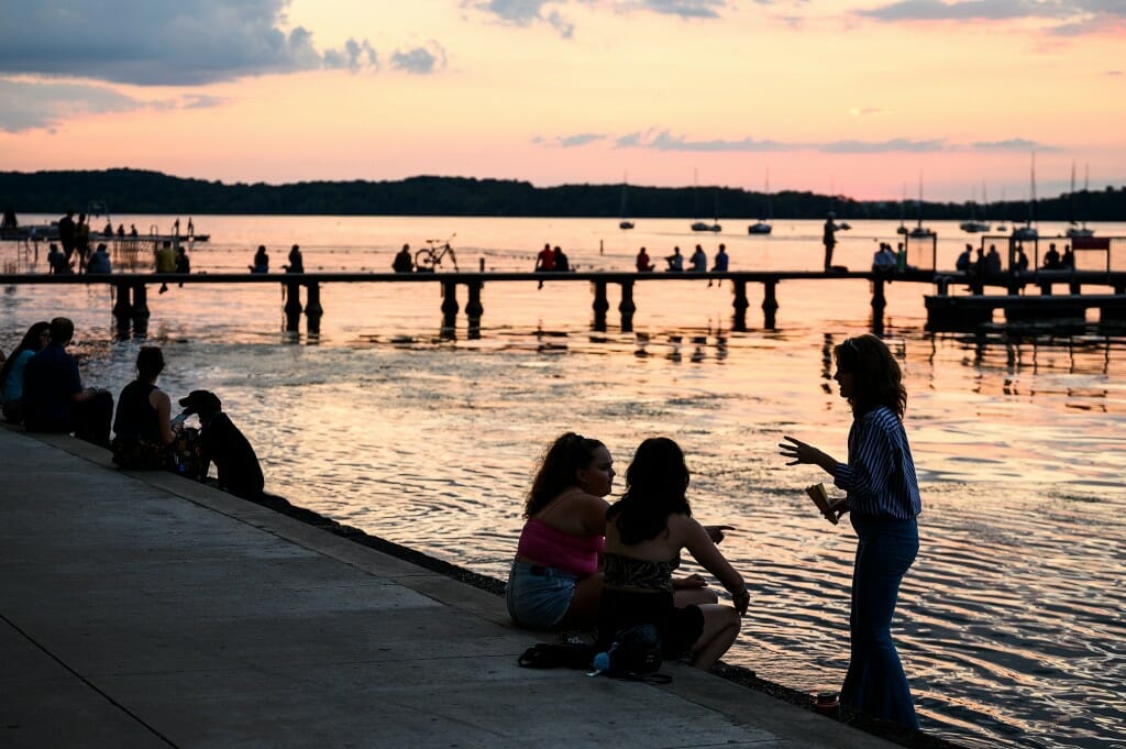 People are silhouetted by the setting sn as they sit along the lake.
