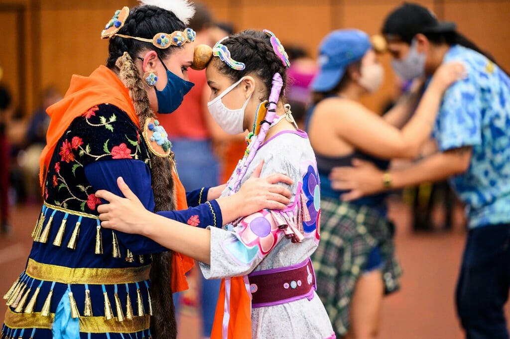 From left to right, Nbiiwakamigkwe of the Leech Lake Band of Ojibwe, and Keja Schreiber of Marten Falls First Nation, embrace for the potato dance – where two dancers hold a potato between their foreheads while attempting to dance with the beat.