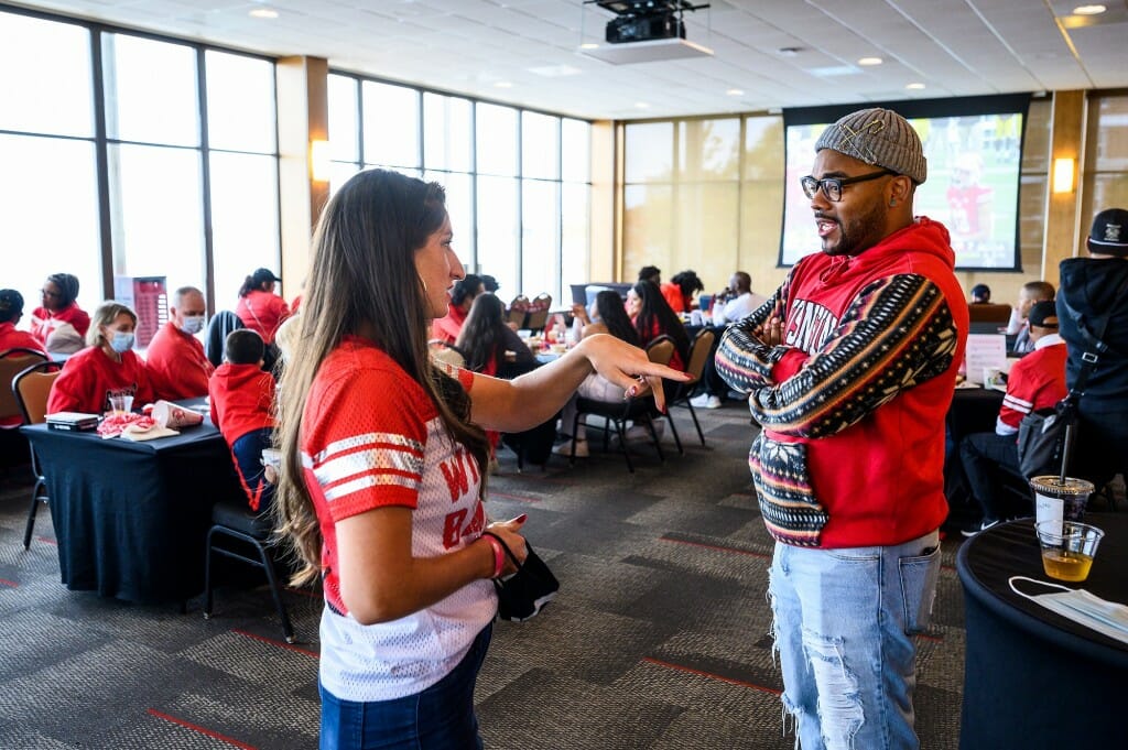 UW–Madison alumni Courtney Luedke (Masters 2011 and Ph. D 2014) and Leonard Taylor (BS 2009 and Masters 2011) catch up while others watch the Wisconsin v. Iowa football game plays on the big screen behind them during the Multicultural Homecoming Game Watch and Tailgate at the Below Alumni Center and Pyle Center.
