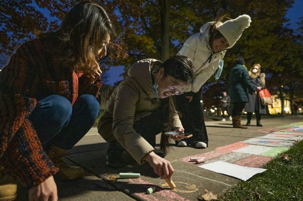 Visiting scholar Yuyang Jiang (center) draws the flag of Mexico in chalk. Also pictured are honorary fellow Di Zhang (left) and undergraduate Intira Setavoraphan (right).
