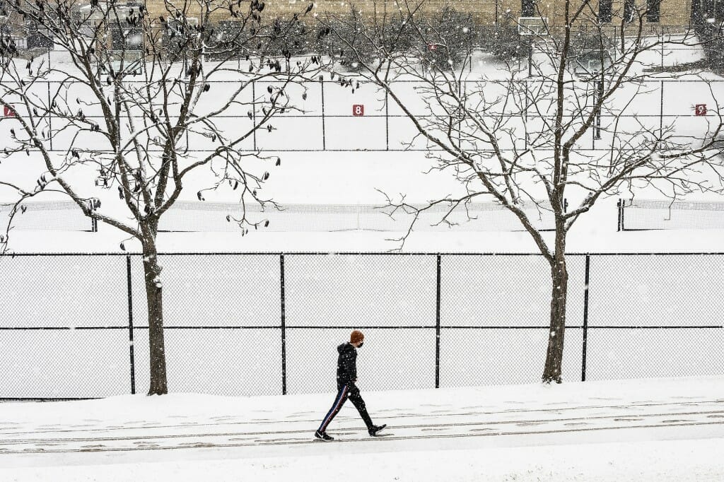 A person walking past snow-covered tennis courts