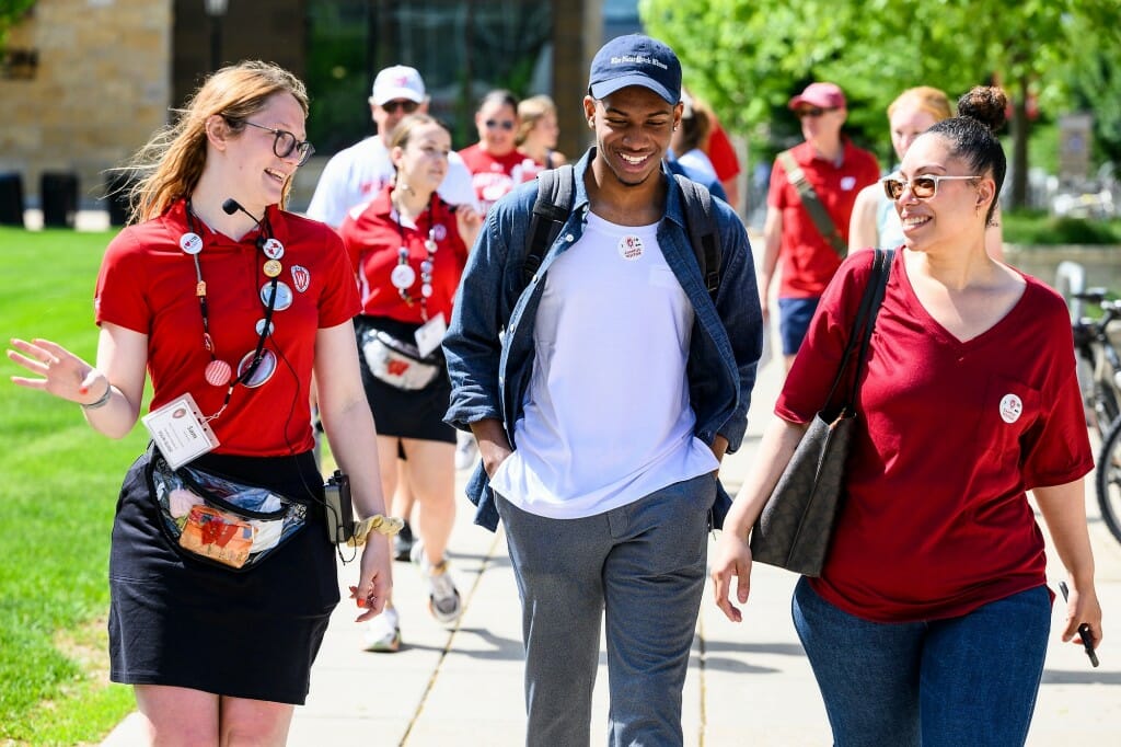 A tour guide leads a prospective student and his mother walking on a sidewalk