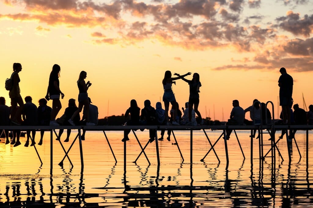People sitting and standing on a pier, looking silhouetted against the sunset