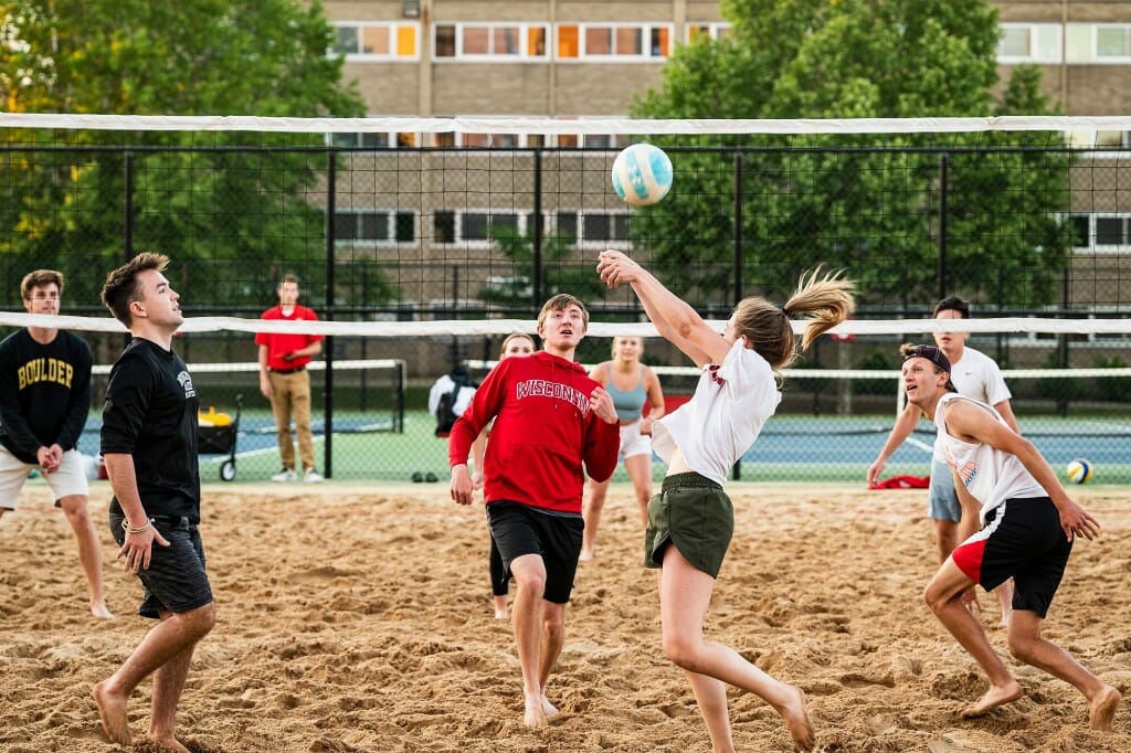 Several students playing volleyball on a sand volleyball court